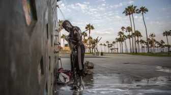 Seorang tunawisma yang telah hidup di jalanan selama 18 tahun, mandi di pancuran umum di Pantai Venesia, California, Amerika Serikat, pada (12/8/2021). [Apu GOMES / AFP]