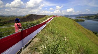 Seorang warga melintasi bendera Merah Putih yang dipasang di bukit Tungku Wiri atau Bukit Teletubies, Kampung Doyo Lama, Distrik Waibu, Kabupaten Jayapura, Papua, Senin (16/8/2021). ANTARA FOTO/Gusti Tanati 