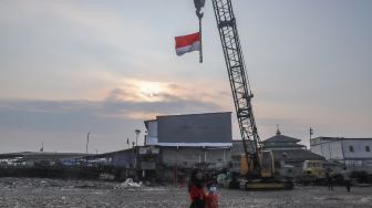 Bendera merah putih dikibarkan melalui alat berat saat upacara bendera HUT RI ke-76 di Belah Kapal, Cilincing, Jakarta Utara, Selasa (17/8/2021). [Suara.com/Alfian Winanto]