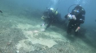 Pemandu selam menunjukkan kepada wisatawan sebuah mosaik dari Villa a Protiro, kota Romawi kuno Baiae yang tenggelam di Taman Bawah Air Baiae, bagian dari situs kompleks Taman Arkeologi Campi Flegrei di Pozzuoli dekat Napoli, Italia, pada (18/8/2021). [Andreas SOLARO / AFP]