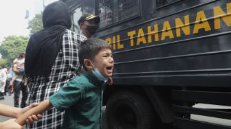 Seorang anak pengungsi Afghanistan menangis saat salah seorang anggota keluarganya dimasukkan ke dalam mobil tahanan di depan Gedung UNHCR, Kebon Sirih, Jakarta, Selasa (24/8/2021). [Suara.com/Angga Budhiyanto]