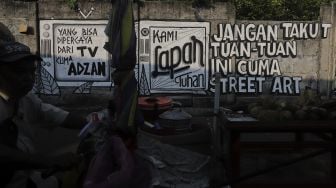 Warga berjalan di dekat mural yang bertuliskan "jangan takut tuan-tuan ini cuma street art" di Jakarta, Rabu (25/8/2021). [Suara.com/Angga Budhiyanto]