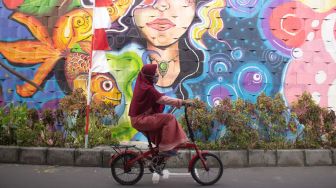 Seorang warga melintas di depan mural di kampung  Pink Kota Tangerang, Jumat (27/8).  ( Suara.com/ Hilal Rauda Fiqry) 
