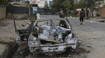 Pejuang Taliban berjaga-jaga di dekat mobil yang rusak setelah beberapa roket ditembakkan di Kabul, Afghanistan, Senin (30/8/2021). [Wakil Kohsar / AFP]