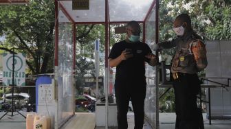 Petugas keamanan mengukur suhu tubuh pengunjung yang akan memasuki Pasar Santa, Jakarta, Kamis (2/9/2021). [Suara.com/Angga Budhiyanto]