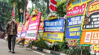 Pegawai gedung melihat karangan bunga yang terpajang di halaman kantor DPRD DKI Jakarta, Jakarta Pusat, Jumat (3/9/2021). [Suara.com/Alfian Winanto]