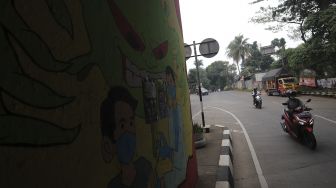 Pengendara sepeda motor melintas di dekat mural bertema COVID-19 di kolong Jalan Tol Lingkar Luar Jakarta, Cipayung, Jakarta Timur, Jumat (3/9/2021). [Suara.com/Angga Budhiyanto]