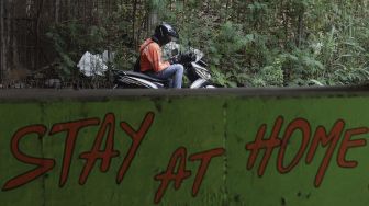 Seorang pengendara sepeda motor berhenti di dekat mural bertema COVID-19 di kolong Jalan Tol Lingkar Luar Jakarta, Cipayung, Jakarta Timur, Jumat (3/9/2021). [Suara.com/Angga Budhiyanto]