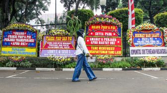 Warga melintasi karangan bunga yang terpajang di halaman kantor DPRD DKI Jakarta, Jakarta Pusat, Jumat (3/9/2021). [Suara.com/Alfian Winanto]