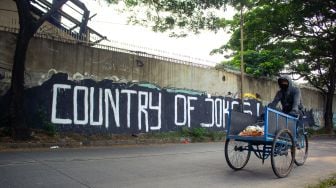 Pengendara becak tengah melintas di mural bertuliskan “ Country of Jokes” di Tangerang, Jumat (3/9).  ( Suara.com/Hilal Rauda Fiqry) 