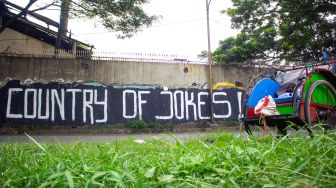 Becak terparkir didepan mural bertuliskan “ Country of Jokes” di Tangerang, Jumat (3/9).  ( Suara.com/Hilal Rauda Fiqry) 