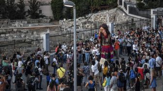 Warga berkumpul di sekitar "Little Amal", boneka raksasa yang menggambarkan seorang gadis pengungsi muda saat diarak di beberapa jalan di Athena, Yunani, pada (2/9/2021). [Louisa GOULIAMAKI / AFP]