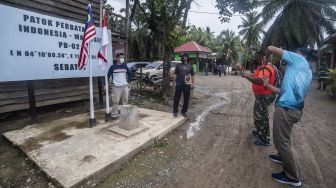 Wisatawan berfoto dengan latar belakang bendera Malaysia-Indonesia di Patok Perbatasan Indonesia-Malaysia, Pulau Sebatik, Senin (13/9/2021).  ANTARA FOTO/Muhammad Adimaja