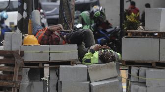 Pekerja beristirahat di sela menyelesaikan proyek revitalisasi trotoar di Jalan Wolter Monginsidi, Kebayoran Baru, Jakarta, Rabu (15/9/2021). [Suara.com/Angga Budhiyanto]