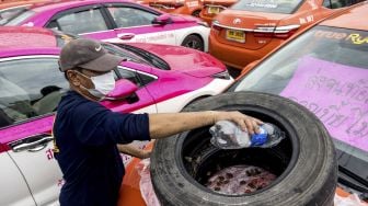 Petugas menuangkan air ke peternakan katak darurat di kap salah satu taksi yang tidak berfungsi karena penurunan bisnis akibat COVID-19 di Bangkok, Thailand, pada (15/9/2021). [Jack TAYLOR / AFP]