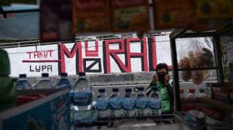 Pengendara ojek daring menunggu penumpang di depan mural yang berisi kritikan di Jakarta Barat, Minggu (19/9/2021).   ANTARA FOTO/Sigid Kurniawan