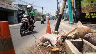 Pengendara sepeda motor melintas di samping tiang miring di Jl Wr Supratman Ciputat Timur, Tangerang Selatan. Rabu (22/9).  [Suara.com/ Hilal Rauda Fiqry]