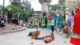 Seorang aktivis menunjukkan aksi teaterikal sambil memegang poster saat melakukan aksi protes terkait perubahan iklim di Kawasan Dukuh Atas, Jakarta Pusat, Minggu (26/9/2021). [Suara.com/Alfian Winanto]