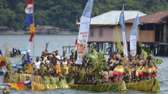 Sejumlah warga dengan pakaian adat menggunakan perahu saati kirab api PON tiba di Dermaga Kalkhote, Danau Sentani, Kabupaten Jayapura, Papua, Sabtu (2/10/2021). [ANTARA FOTO/Fauzan]