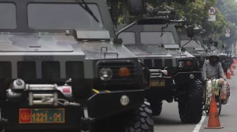 Pedagang keliling melintas di dekat deretan alutsista yang terparkir di Jalan Medan Merdeka Barat, Jakarta, Senin (4/10/2021). [Suara.com/Angga Budhiyanto]