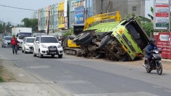 Sejumlah pengendara roda dua melintas di samping truk yang terperosok galian pipa PDAM di jalan raya Legok, Kabupaten Tangerang, Banten, Kamis (7/10).  [Suara.com/ Hilal Rauda Fiqry] 