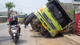 Sejumlah pengendara roda dua melintas di samping truk yang terperosok galian pipa PDAM di jalan raya Legok, Kabupaten Tangerang, Banten, Kamis (7/10).  [Suara.com/ Hilal Rauda Fiqry] 