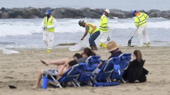 Pengunjung duduk di kursi pantai saat kru pembersihan bekerja di Pantai Newport, California, pada (7/10/2021). [Frederic J. BROWN / AFP]