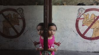 Seorang anak berdiri di dekat mural larangan merokok di RW.06 Kelurahan Kayu Manis, Matraman, Jakarta, Jumat (8/10/2021). [Suara.com/Angga Budhiyanto]