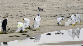 Seorang pengunjung duduk di kursi pantai saat kru pembersihan bekerja di Pantai Newport, California, pada (7/10/2021). [Frederic J. BROWN / AFP]