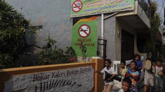 Sejumlah anak berjalan melintasi mural larangan merokok di RW.06 Kelurahan Kayu Manis, Matraman, Jakarta, Jumat (8/10/2021). [Suara.com/Angga Budhiyanto]