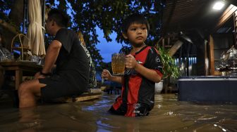 Pengunjung membawa minuman di Kafe Antik Chaopraya, saat air banjir dari Sungai Chao Phraya mengalir ke restoran di provinsi Nonthaburi, Bangkok, Thailand, pada (7/10/2021). [Lillian SUWANRUMPHA / AFP]