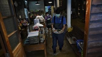 Seorang karyawan yang menyajikan makanan di Kafe Antik Chaopraya, saat air banjir dari Sungai Chao Phraya mengalir ke restoran di provinsi Nonthaburi, Bangkok, Thailand, pada (7/10/2021). [Lillian SUWANRUMPHA / AFP]