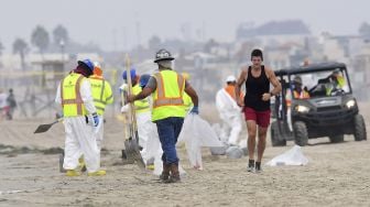 Seorang pengunjung berlari melewati kru pembersihan yang bekerja di Pantai Newport, California, pada (7/10/2021). [Frederic J. BROWN / AFP]