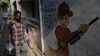 Warga berjalan melintasi mural larangan merokok di RW.06 Kelurahan Kayu Manis, Matraman, Jakarta, Jumat (8/10/2021). [Suara.com/Angga Budhiyanto]