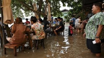 Pengunjung menikmati makan malam di Kafe Antik Chaopraya, saat air banjir dari Sungai Chao Phraya mengalir ke restoran di provinsi Nonthaburi, Bangkok, Thailand, pada (7/10/2021). [Lillian SUWANRUMPHA / AFP]