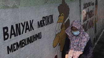 Warga berjalan melintasi mural larangan merokok di RW.06 Kelurahan Kayu Manis, Matraman, Jakarta, Jumat (8/10/2021). [Suara.com/Angga Budhiyanto]