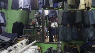 Refleksi pedagang merapikan pakaian bekas layak pakai (thrifting) di Pasar Kebayoran Lama, Jakarta, Rabu (13/10/2021). [Suara.com/Angga Budhiyanto]