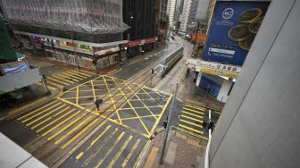 Seorang pejalan kaki melintasi jalan yang kosong di kawasan pusat bisnis di Hong Kong, pada (13/10/2021). [PETER PARKS / AFP]