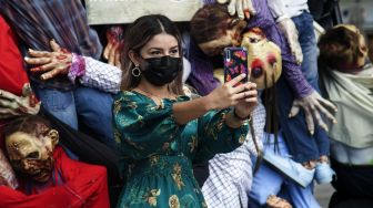 Seorang warga berswafoto dengan sosok zombie yang dipamerkan di pusat perbelanjaan sebagai bagian dari dekorasi Musim Halloween di San Pedro Garza, Nuevo Leon, Meksiko, pada (22/10/2021). [JULIO CESAR AGUILAR / AFP]