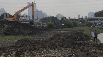 Warga berjalan di dekat alat berat yang melakukan pengerukan sedimen lumpur di sepanjang aliran Kanal Banjir Barat di kawasan Tanah Abang, Jakarta, Jumat (29/10/2021). [Suara.com/Angga Budhiyanto]