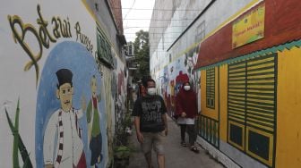 Warga berjalan melintasi mural bertema budaya Betawi di kawasan Kampung Sentra Kreatif, RW 006 Kota Bambu Selatan, Palmerah, Jakarta, Rabu (3/11/2021). [Suara.com/Angga Budhiyanto]