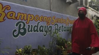 Warga berjalan melintasi mural bertema budaya Betawi di kawasan Kampung Sentra Kreatif, RW 006 Kota Bambu Selatan, Palmerah, Jakarta, Rabu (3/11/2021). [Suara.com/Angga Budhiyanto]