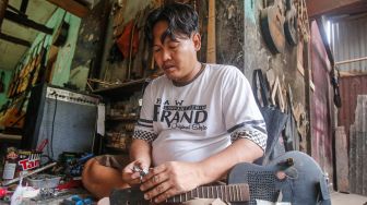 Pekerja menyelesaikan pembuatan gitar di sentra produksi dan reparasi gitar Pak Manto di Jalan Langgar II, Pejaten Timur, Pasar Minggu, Jakarta Selatan, Jumat (5/11/2021). [Suara.com/Alfian Winanto]