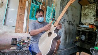 Pekerja menyelesaikan pembuatan gitar di sentra produksi dan reparasi gitar Pak Manto di Jalan Langgar II, Pejaten Timur, Pasar Minggu, Jakarta Selatan, Jumat (5/11/2021). [Suara.com/Alfian Winanto]