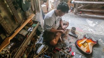 Pekerja menyelesaikan pembuatan gitar di sentra produksi dan reparasi gitar Pak Manto di Jalan Langgar II, Pejaten Timur, Pasar Minggu, Jakarta Selatan, Jumat (5/11/2021). [Suara.com/Alfian Winanto]