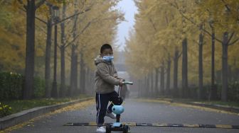 Seorang anak mengenakan masker saat mengendarai skuter di sepanjang jalan pada hari yang berkabut dan tercemar di Beijing, China, Sabtu (6/11/2021). [JADE GAO / AFP]