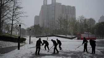 Pekerja menyekop salju di depan sebuah mal di Beijing, China, Minggu (7/11/2021). [NOEL CELIS / AFP]