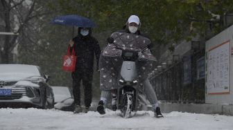 Orang-orang bepergian di jalan saat salju turun di Beijing, China, Minggu (7/11/2021). [NOEL CELIS / AFP]