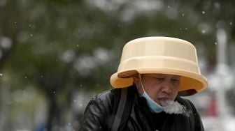Seorang warga menggunakan baskom air sebagai topi saat salju turun di Beijing, China, Minggu (7/11/2021). [NOEL CELIS / AFP]