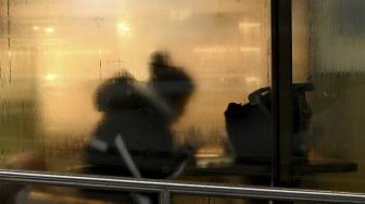 Seorang warga duduk di dalam kedai kopi saat salju turun di Beijing, China, Minggu (7/11/2021). [NOEL CELIS / AFP]